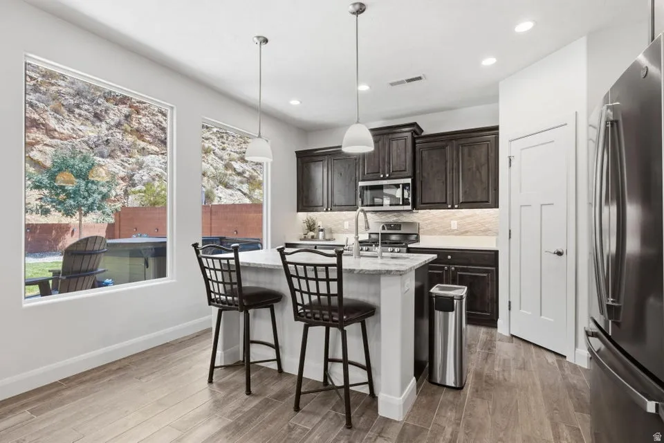Kitchen featuring dark wood cabinetry, stainless steel appliances, a center island with pendant lighting, and wood-finish flooring