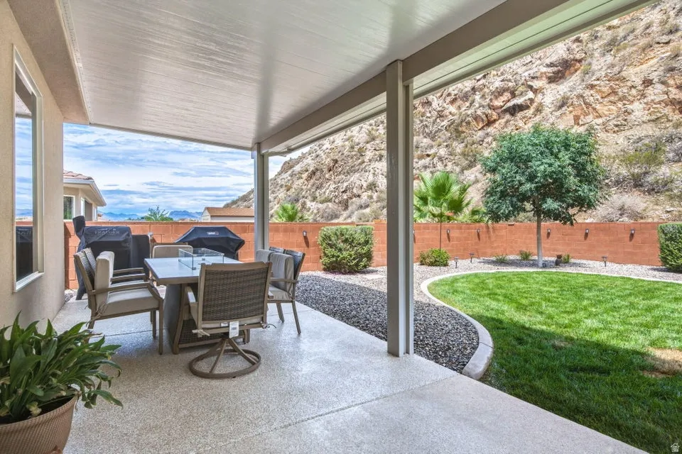Covered patio with integrated dining and lounge seating overlooking manicured lawn, mature landscaping, and brick privacy walls