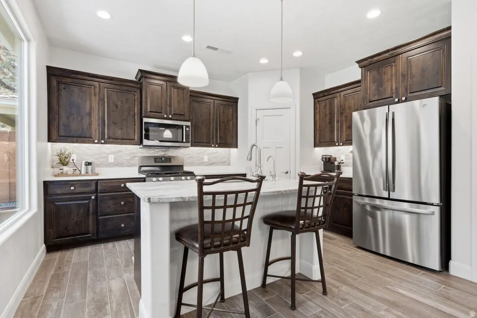 Contemporary kitchen featuring dark wood cabinetry, stainless steel appliances, a center island with seating, pendant lighting, and wood-finish flooring