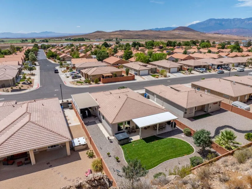 Aerial perspective of a neighborhood featuring single-story homes with tile roofs, a private backyard with a manicured lawn, and a covered patio