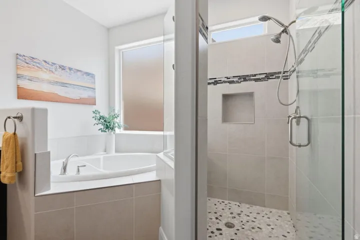 Spa-inspired primary bathroom featuring a soaking tub with deck-mounted faucet, a walk-in shower with frameless glass enclosure and rainfall showerhead, neutral tile finishes, and a pebble-textured shower floor