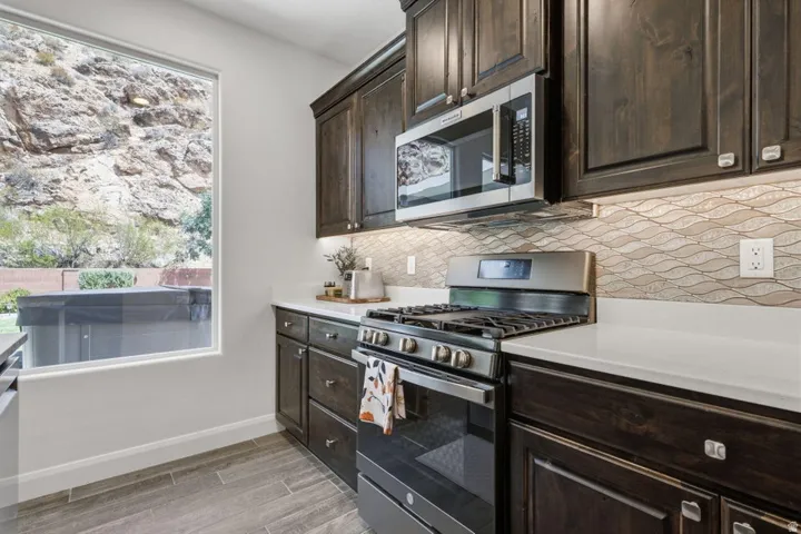 Modern kitchen featuring dark wood cabinetry with stainless steel hardware, a professional-grade gas range with dual ovens, and a built-in microwave