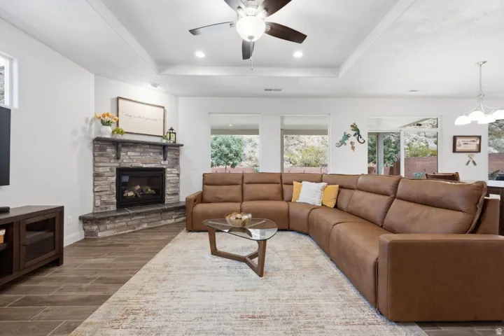 Spacious living area featuring a stone-clad fireplace with mantel, tray ceiling, and wood-finish flooring