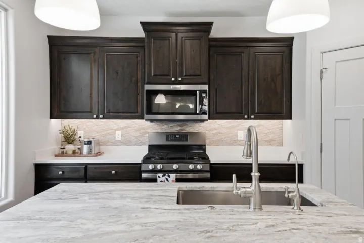 Gourmet kitchen featuring dark wood cabinetry with polished hardware, a black gas cooktop with stainless steel range hood, and a built-in microwave