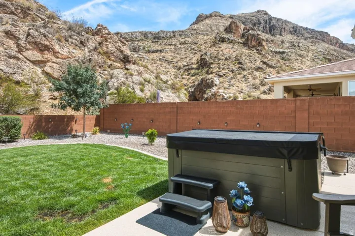 Expansive backyard featuring a hot tub, mature trees, manicured lawn, and a privacy wall