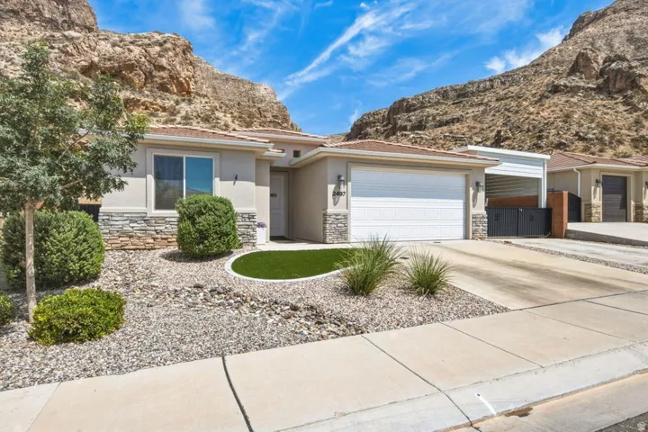 Exterior featuring a stucco finish with stone accents, a two-car garage, a concrete driveway, and an artificial turf landscape element