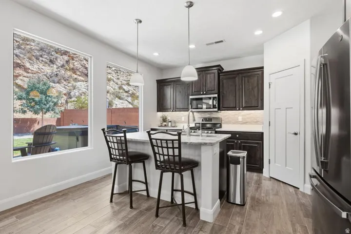 Kitchen featuring dark wood cabinetry, stainless steel appliances, a center island with pendant lighting, and wood-finish flooring