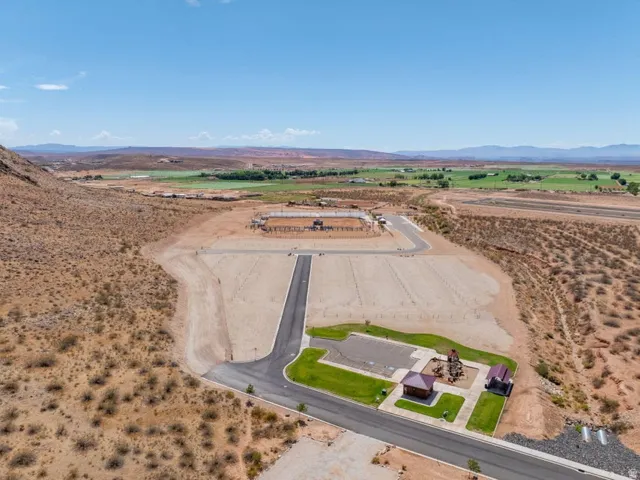 Expansive land parcel with paved road access, a green space featuring a playground structure and covered shelter, and a backdrop of distant green fields and mountains