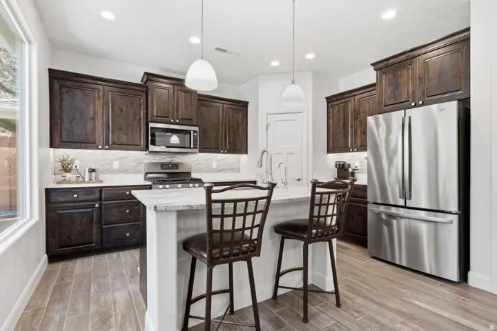 Contemporary kitchen featuring dark wood cabinetry, stainless steel appliances, a center island with seating, pendant lighting, and wood-finish flooring