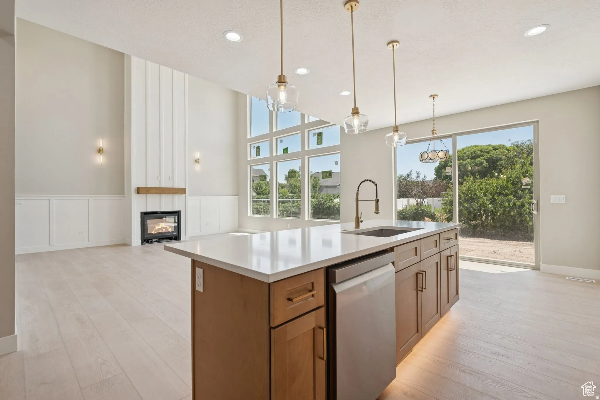 Gourmet kitchen featuring a substantial wood-finish island with integrated sink and stainless steel appliances, white quartz countertops, pendant lighting, recessed ceiling lights, and expansive windows overlooking the outdoor landscape