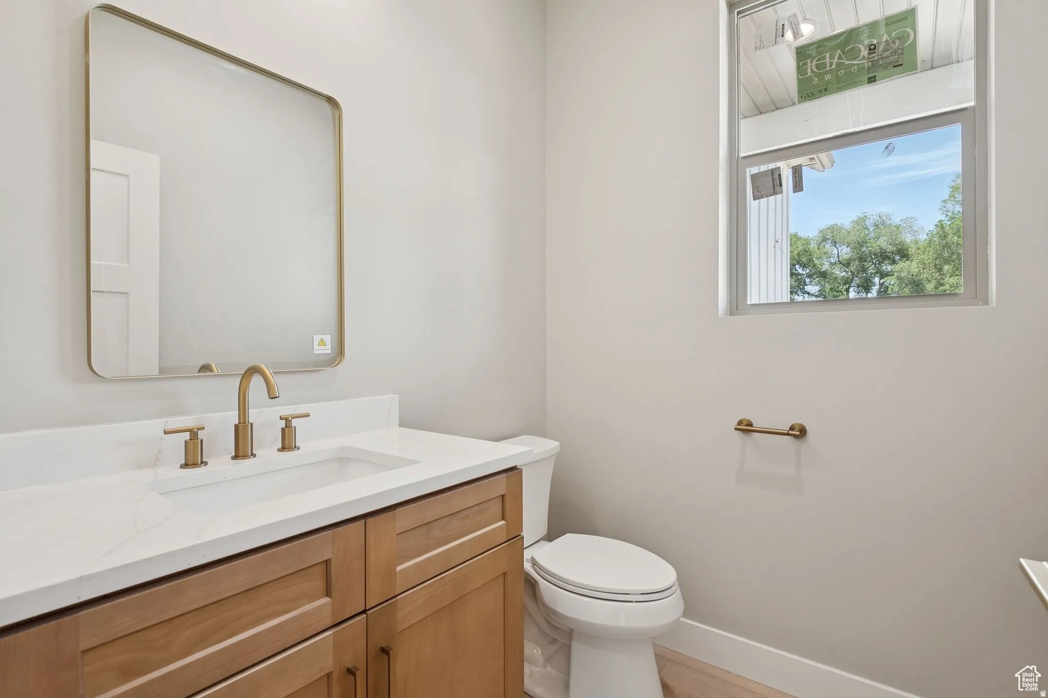 Bathroom featuring a light wood vanity, white countertop, brushed brass fixtures, and a rectangular mirror