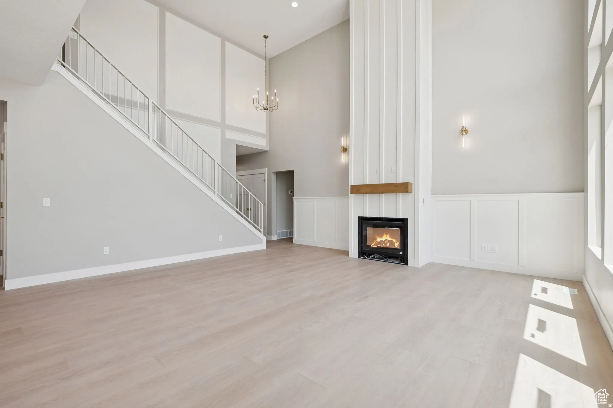Two-story living area featuring a prominent fireplace with a wood mantel, light wood-finish flooring, and a contemporary chandelier
