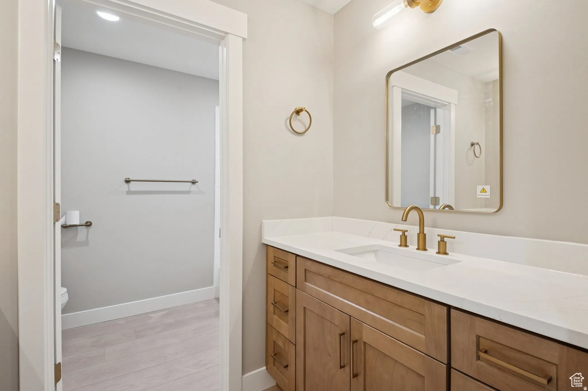 Spa-inspired bathroom featuring a wood-finish vanity with dual drawers, white quartz countertop, and brass-finished faucet and hardware