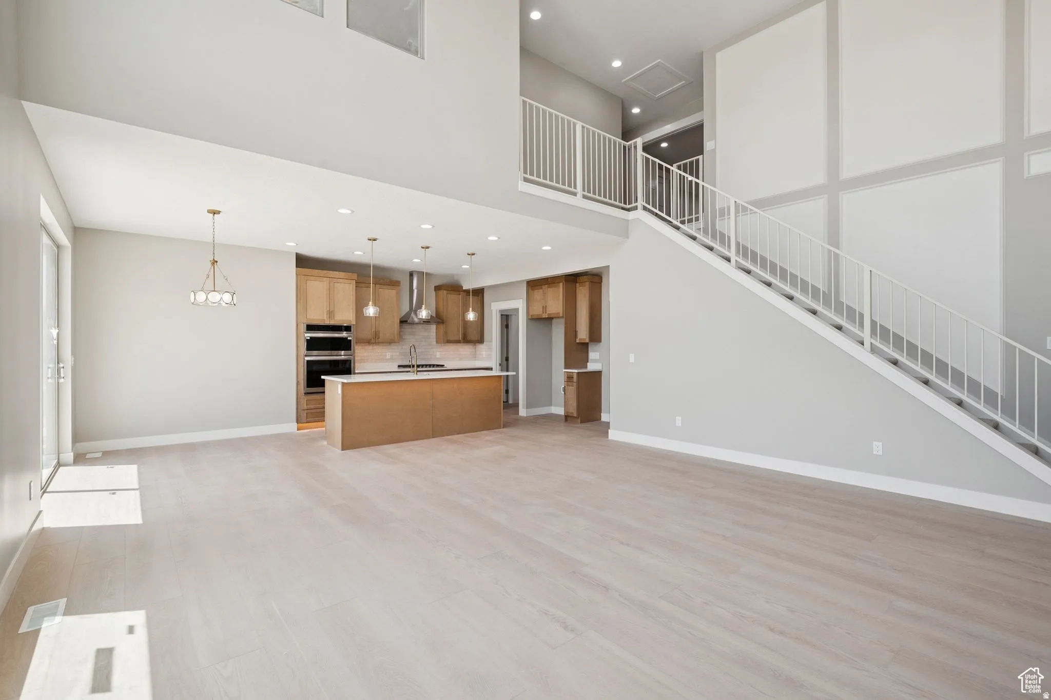 Open-concept living space featuring wood-finish flooring, a two-story ceiling, and a modern staircase with white railing