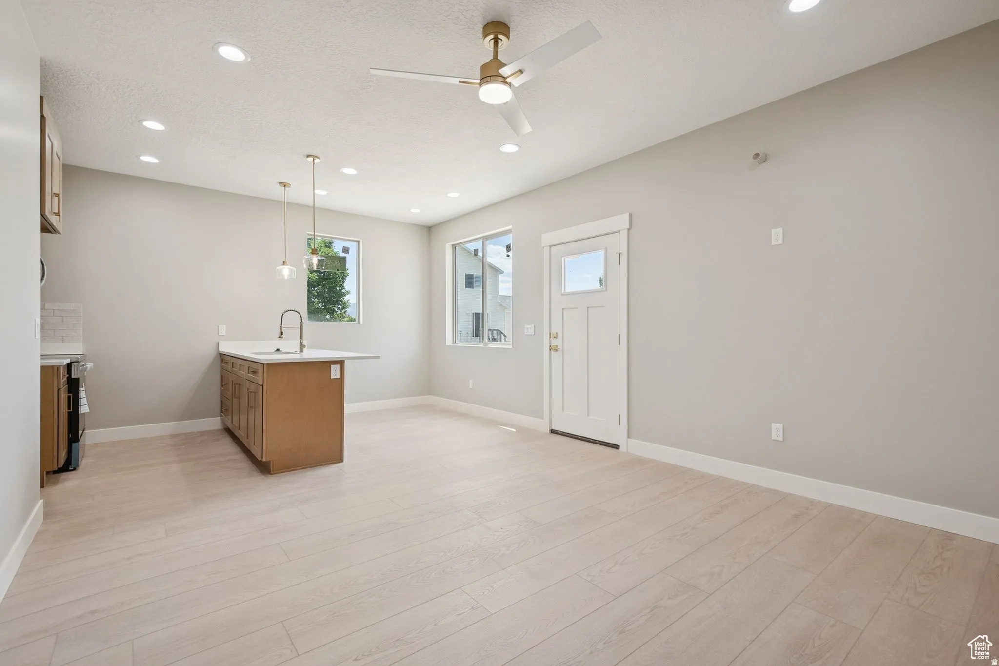 Bright and spacious open-concept space featuring light wood-finish flooring throughout, recessed ceiling lighting, and a ceiling fan