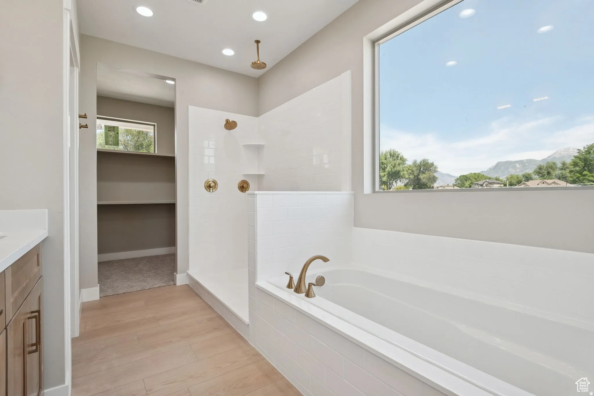 Spa-inspired primary bathroom featuring a freestanding soaking tub with brushed bronze fixtures, white subway tile surround, and wood-finish flooring