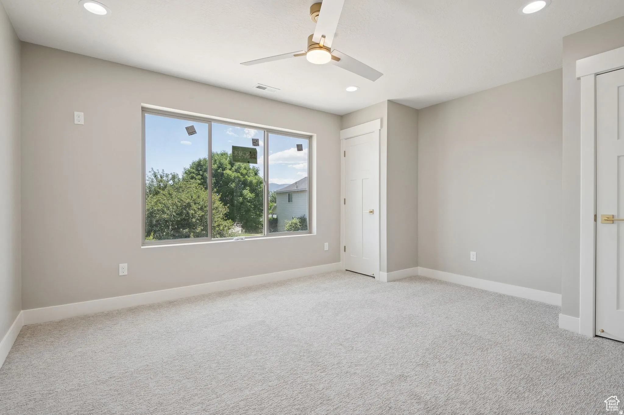 Spacious bedroom with abundant natural light from large multi-pane windows, neutral carpet flooring, recessed ceiling lighting, ceiling fan, and direct access to a hallway