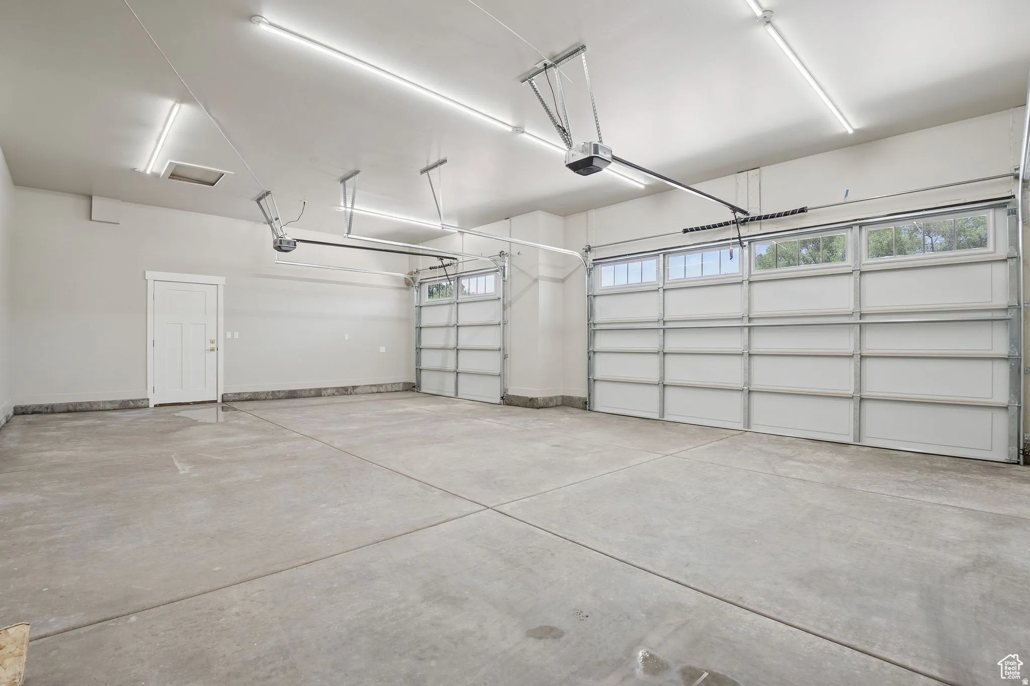 Spacious three-car garage featuring polished concrete flooring, overhead LED lighting, and dual garage door openers with transom windows allowing natural light throughout the space