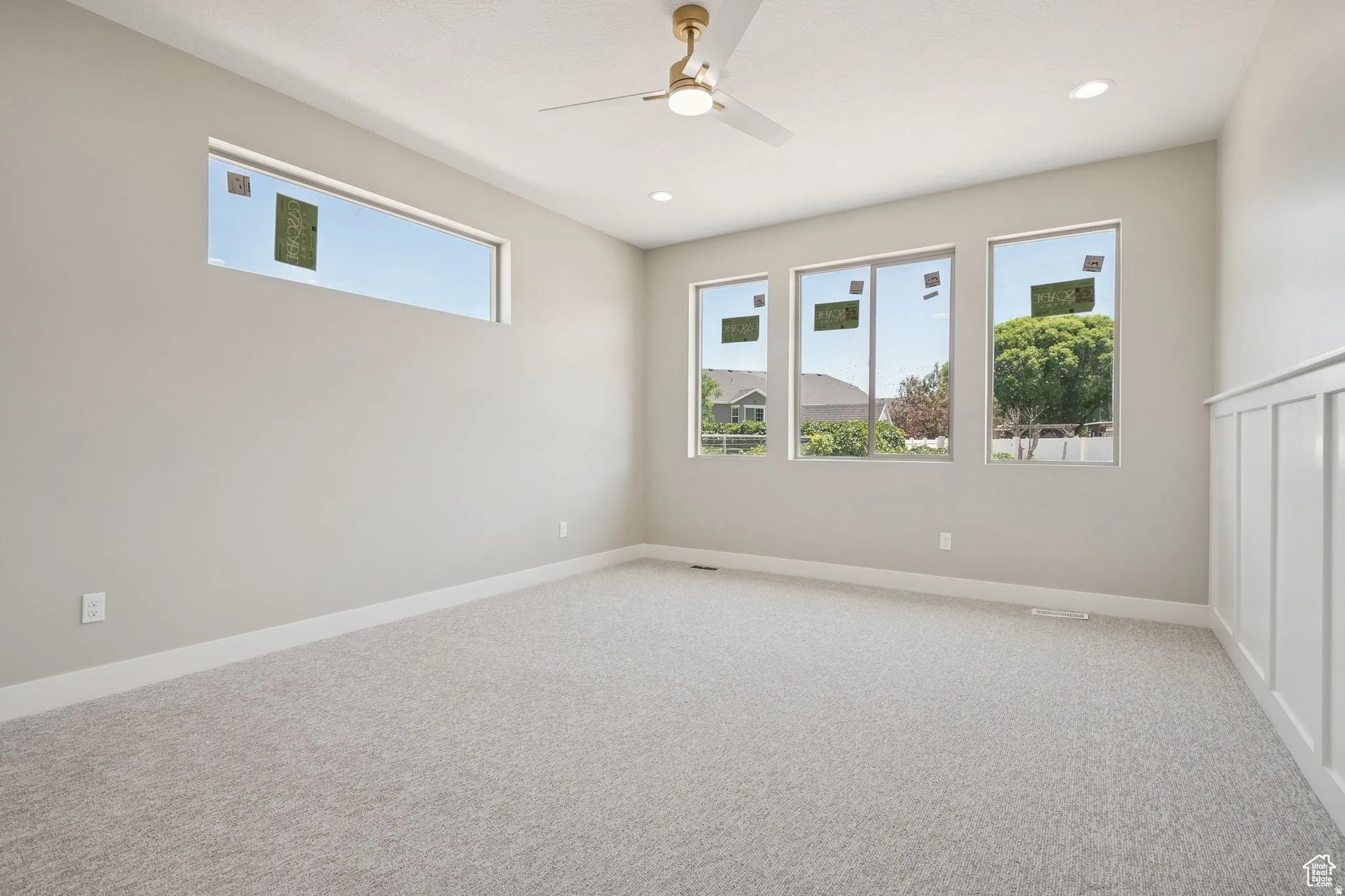 Bright and spacious bedroom showcasing abundant natural light through multiple large windows, neutral carpet flooring, and recessed ceiling lighting