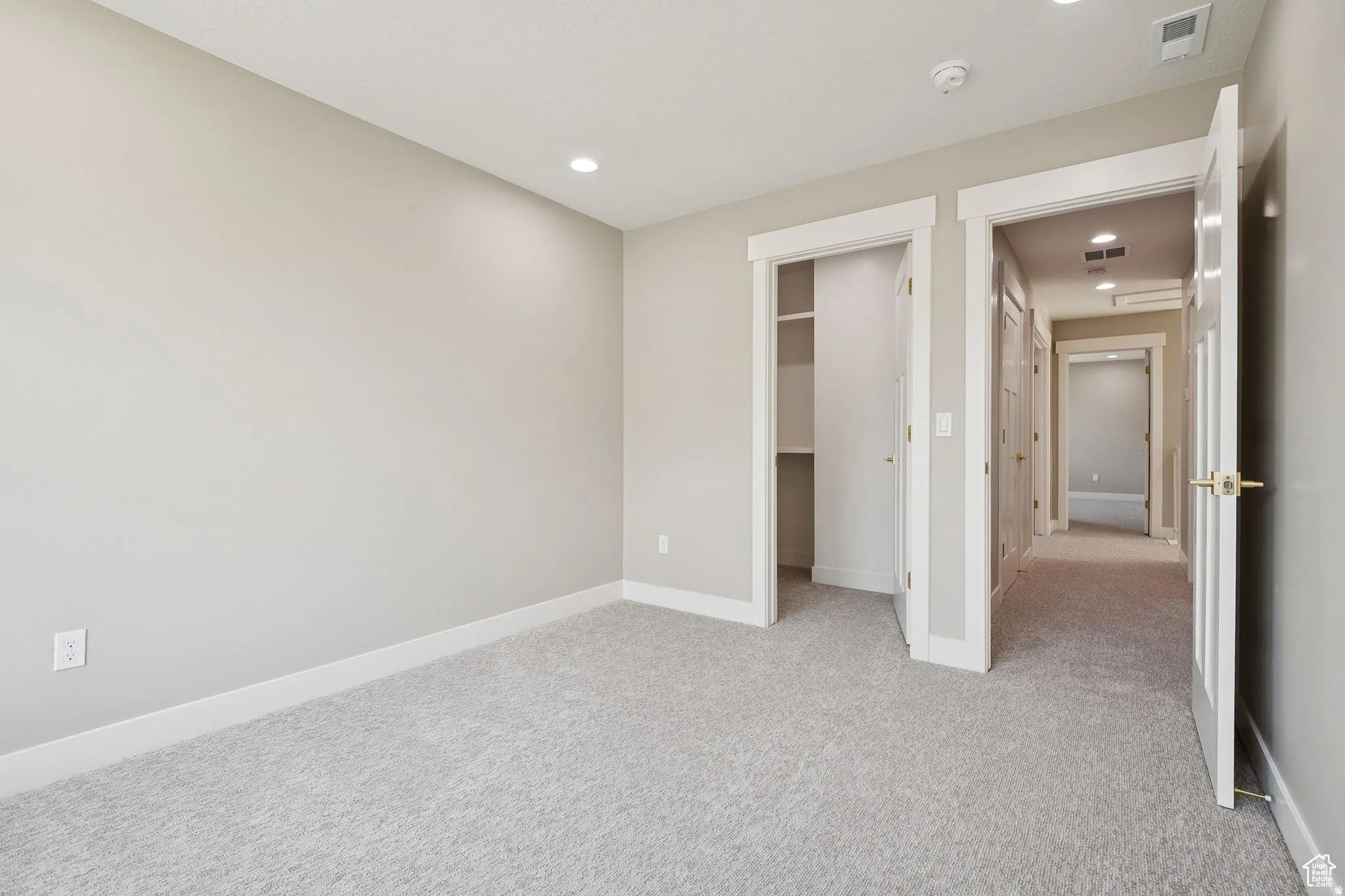Spacious bedroom featuring neutral wall finishes, plush carpet flooring, recessed ceiling lighting, and dual closet access with white-trimmed doors