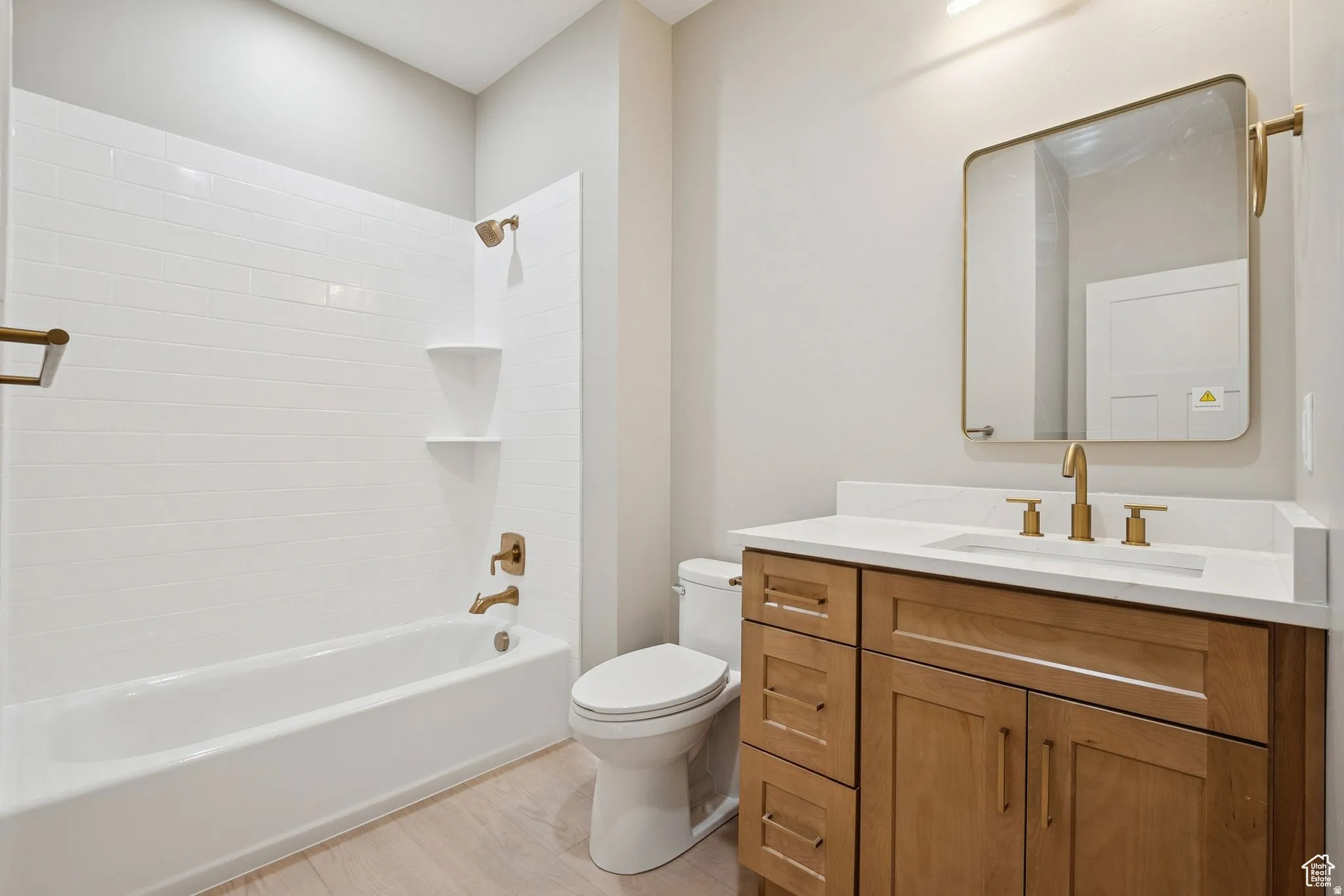 Spa-inspired bathroom featuring a wood-finish vanity with dual brass fixtures, white quartz countertop, and ample storage