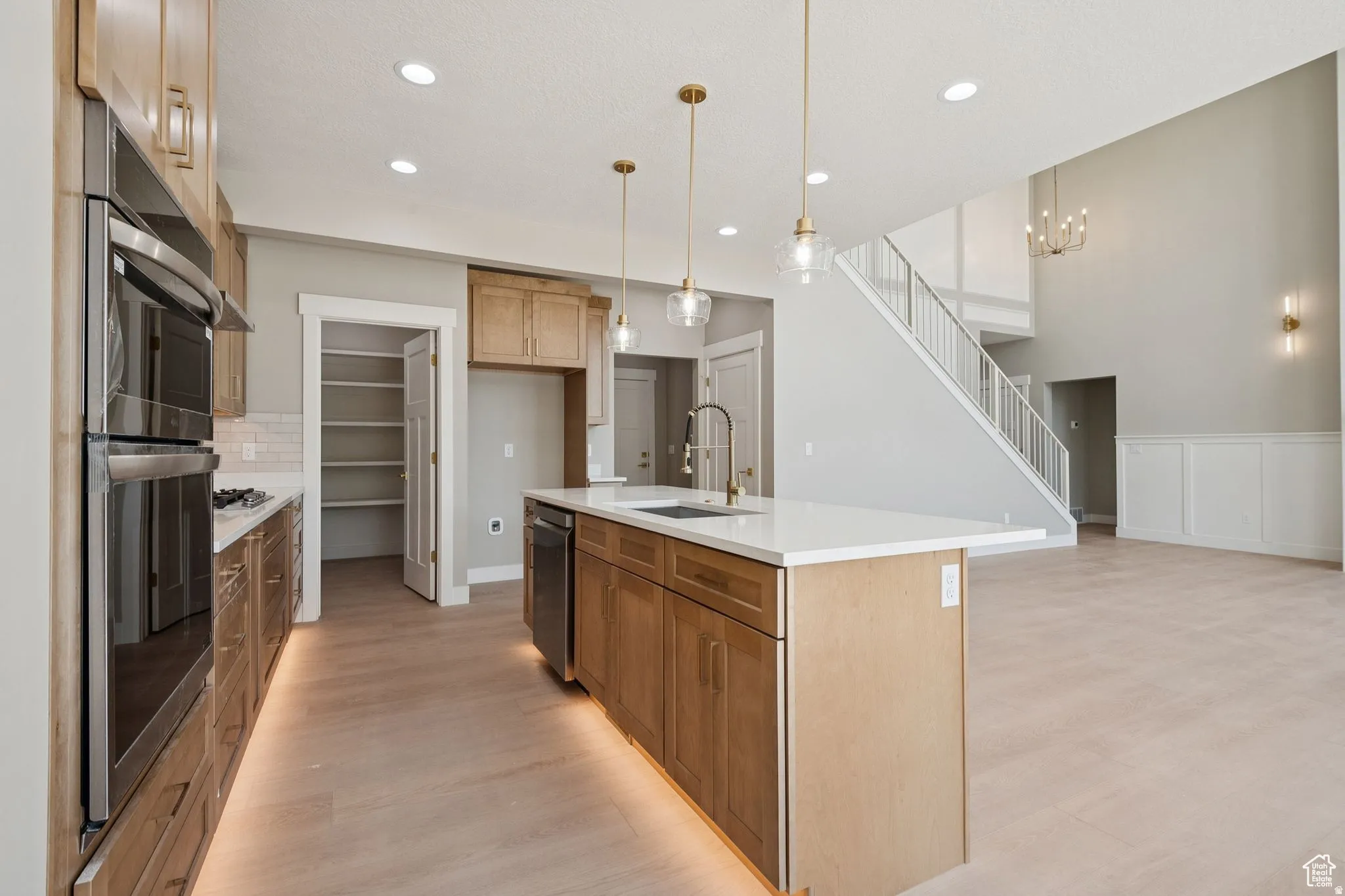 Chef's kitchen featuring a substantial island with white quartz countertop, custom wood cabinetry, stainless steel built-in appliances including double wall ovens, and pendant lighting