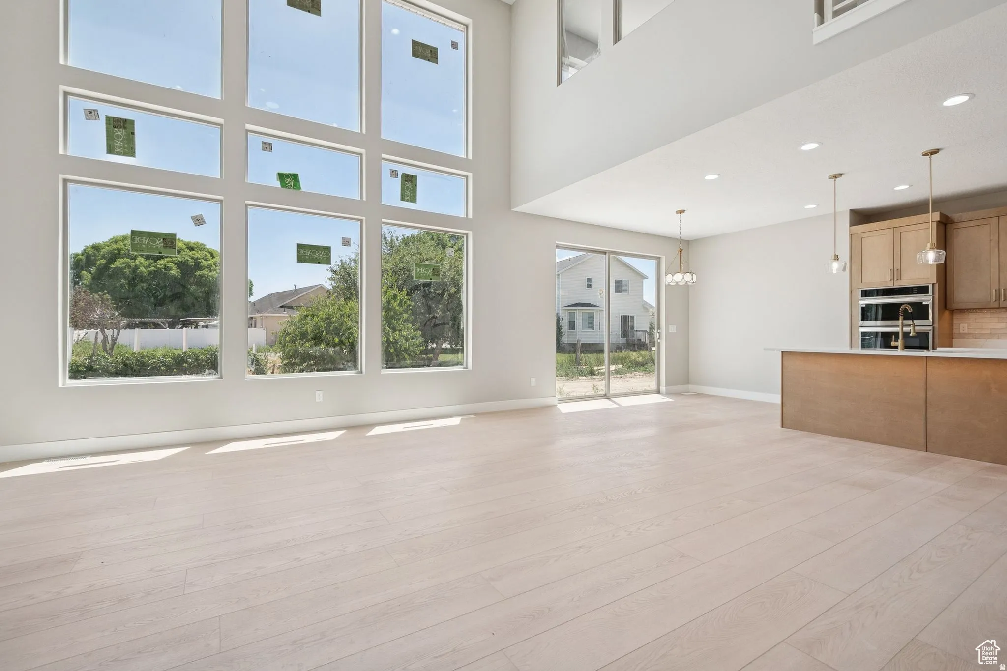 Two-story living area featuring a multi-pane window wall, light wood-finish flooring, recessed ceiling lights, and a sliding glass door