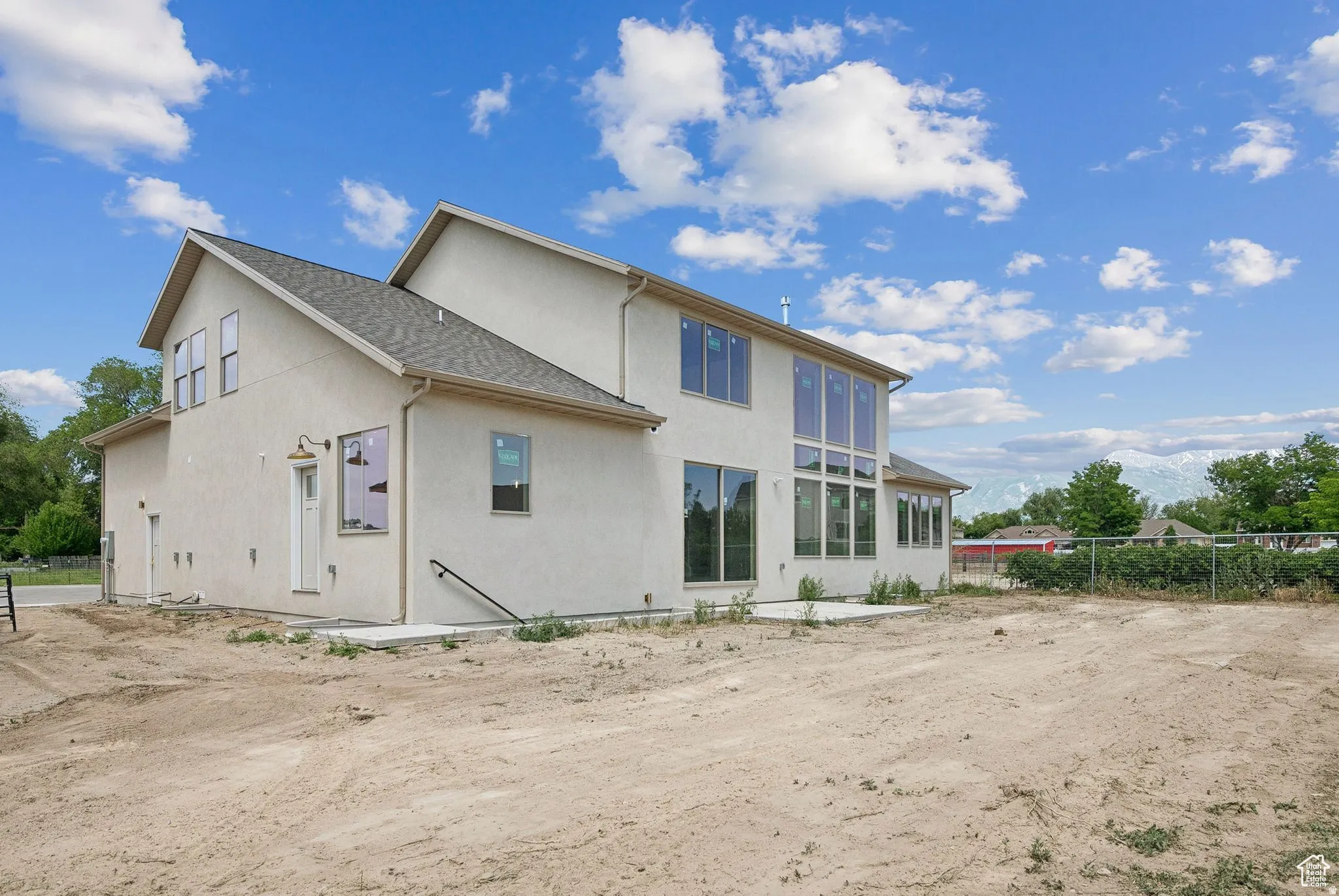 Contemporary stucco exterior featuring a multi-level roofline, extensive window arrays, a rear patio, and partial mountain scenery