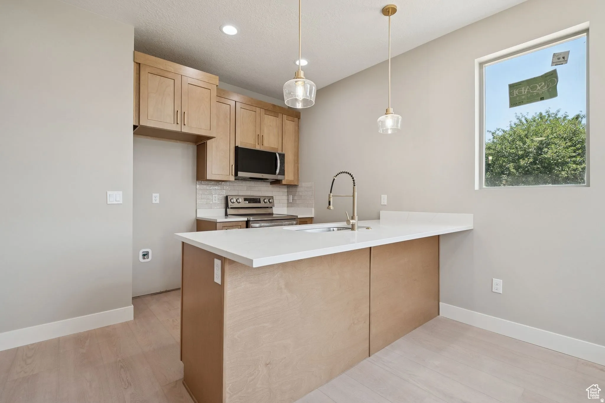 Modern kitchen featuring light wood-finish cabinetry, stainless steel appliances, a white tile backsplash, and light-toned countertops