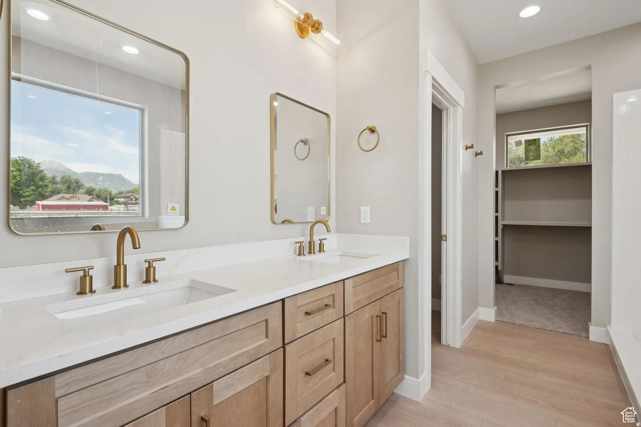 Primary Bathroom featuring a wood-finish vanity with dual sinks, white quartz countertop, brushed brass fixtures, and framed mirrors with brass accents