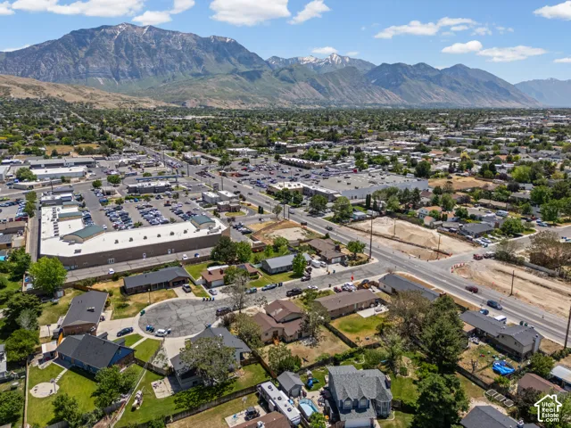 Aerial view showcasing this property's prime location within an established neighborhood, featuring mature landscaping, manicured grounds with multiple trees, and proximity to commercial corridors and mountain backdrop