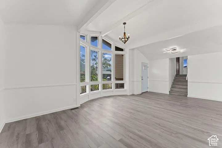 Bright, open living space showcasing hardwood-finish flooring, soaring vaulted ceilings with exposed beams, and abundant natural light from multi-pane windows