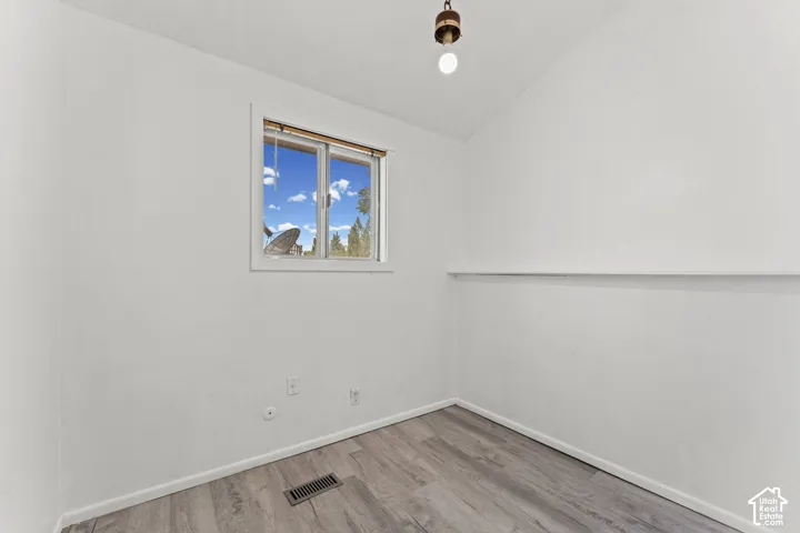 Bright secondary bedroom featuring wood-finish flooring, clean white walls, and a large window with natural light and blue sky views