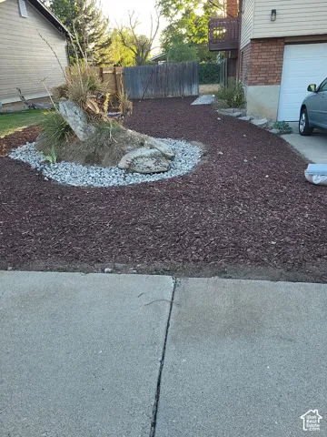 Landscaped front yard featuring decorative rocks, mature plantings, and wood chip ground cover