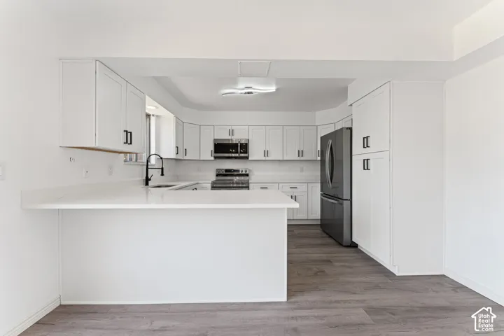 Modern kitchen featuring white cabinetry with brushed nickel hardware, quartz countertops, a large waterfall-edge island, and stainless steel appliances including a gas range and French-door refrigerator