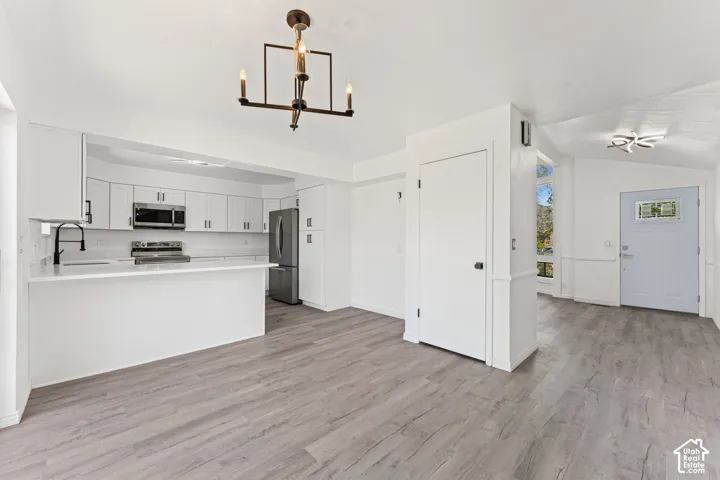 Open-concept kitchen and living area featuring white cabinetry with stainless steel appliances, a waterfall-edge island with seating, wood-finish flooring throughout, recessed lighting, and abundant natural light from multiple windows and glass doors