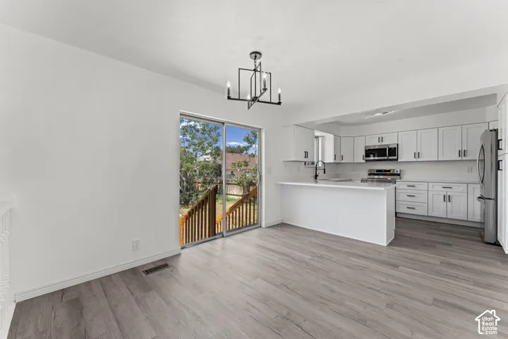 Open-concept living and dining area featuring wood-finish flooring, white cabinetry with stainless steel appliances, a central island with white quartz countertop, and glass sliding doors opening to a wooden deck with tree-lined surroundings