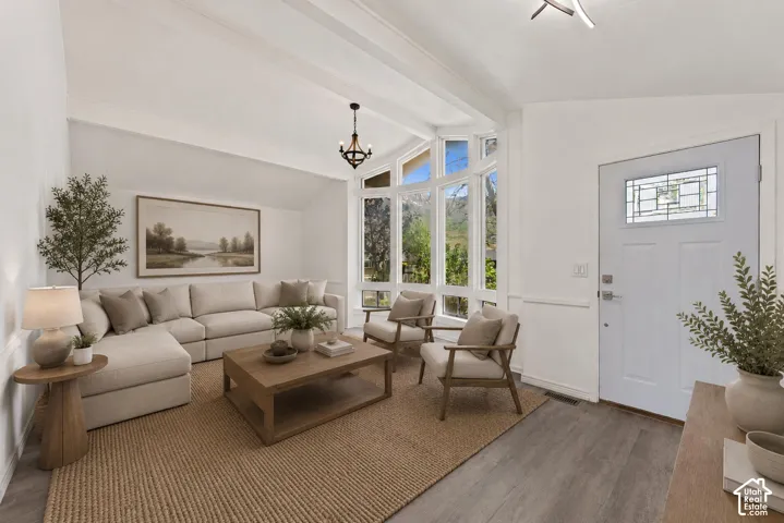 Living area featuring vaulted ceilings with exposed beams, bay windows, wood-finish flooring, and a white entry door with leaded glass