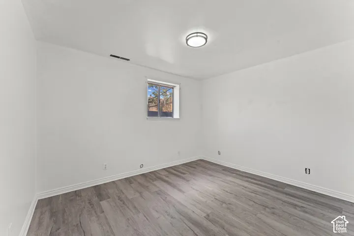 Spacious room featuring pristine white walls, recessed ceiling lighting, and engineered wood-finish flooring in a warm gray tone