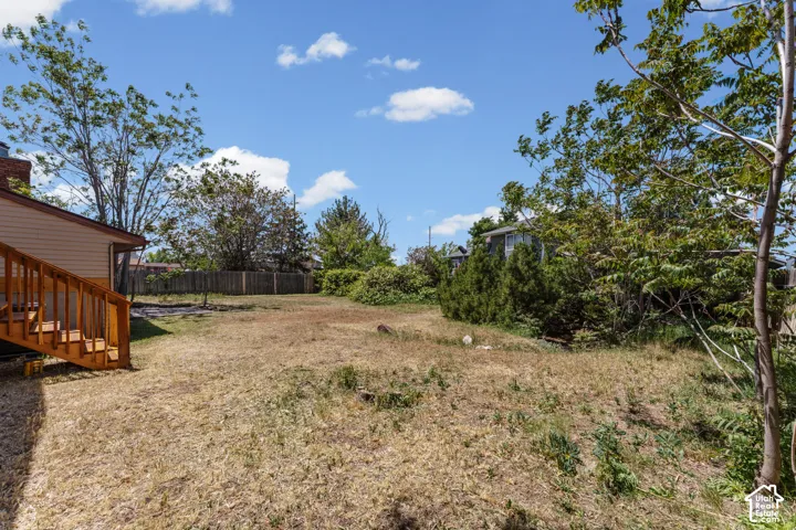 Expansive rear yard featuring natural landscaping, mature trees, and a wood privacy fence