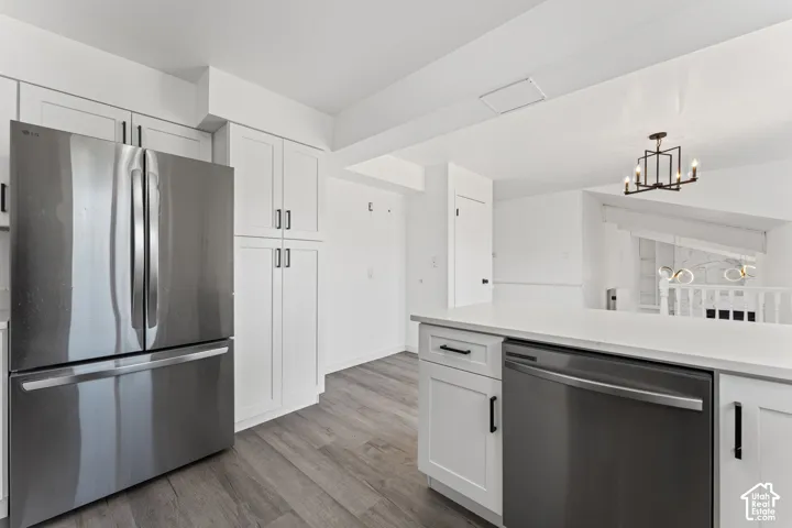 Modern kitchen featuring stainless steel French-door refrigerator, white cabinetry with brushed nickel hardware, wood-finish flooring, and a large island with black base cabinetry and stainless steel appliances