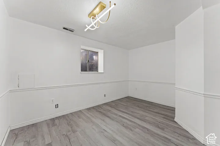 Spacious room featuring newly installed wood-finish flooring, crisp white walls with coordinating chair rail molding, and recessed lighting