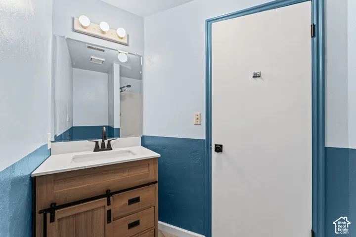 Bathroom vanity featuring a light wood-finish base with barn door style cabinetry, a white countertop with integrated sink, and a matte black faucet