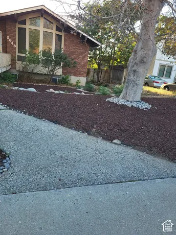 Brick exterior with a large bay window, featuring an exposed aggregate concrete walkway, and a landscaped garden bed with mulch and decorative stones