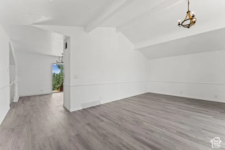 Spacious interior featuring wood-finish flooring, vaulted ceilings with exposed beams, and a brass chandelier