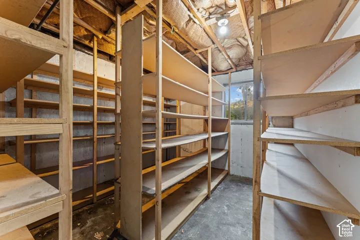 Spacious storage room featuring extensive built-in wooden shelving throughout, concrete flooring, exposed beam ceiling structure, and abundant natural light from overhead skylights and windows