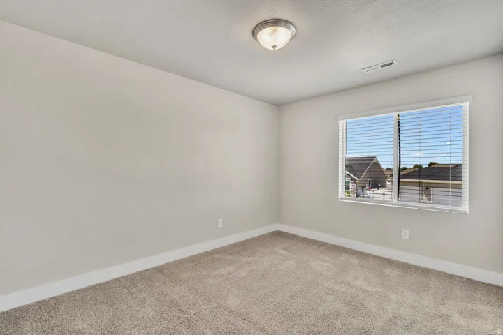 Bright secondary bedroom featuring neutral wall finishes, plush carpeting, and abundant natural light from a large dual-pane window