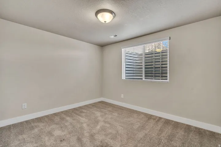 Room featuring light-toned walls, textured carpeting, a window with blinds, and a semi-flush ceiling light fixture
