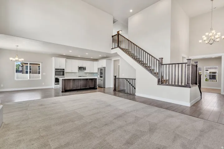 Open-concept great room showcasing soaring ceilings, a floating staircase with black metal railings, and abundant natural light from recessed fixtures and pendant lighting