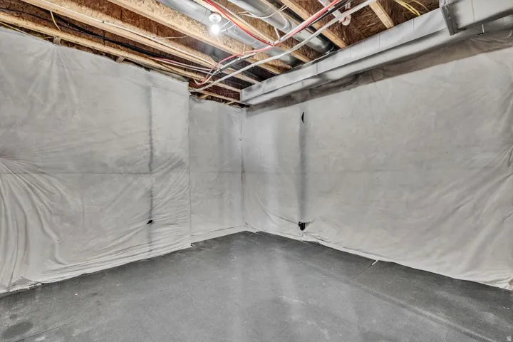 Unfinished basement space with polished concrete flooring, exposed ceiling infrastructure, and plastic vapor barrier wall coverings